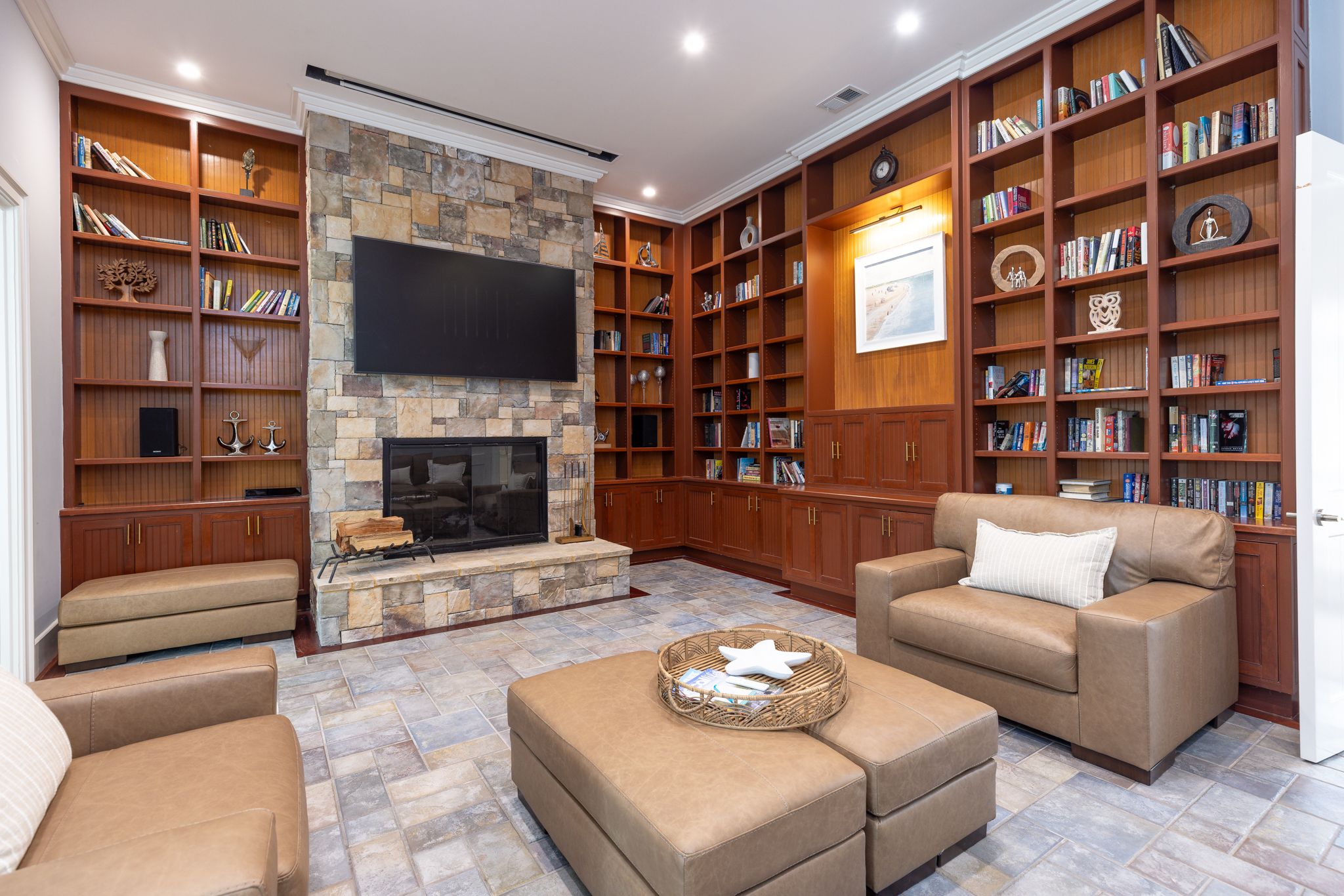 Library with stone fireplace, full wood bookshelves, and leather seating for evening sessions