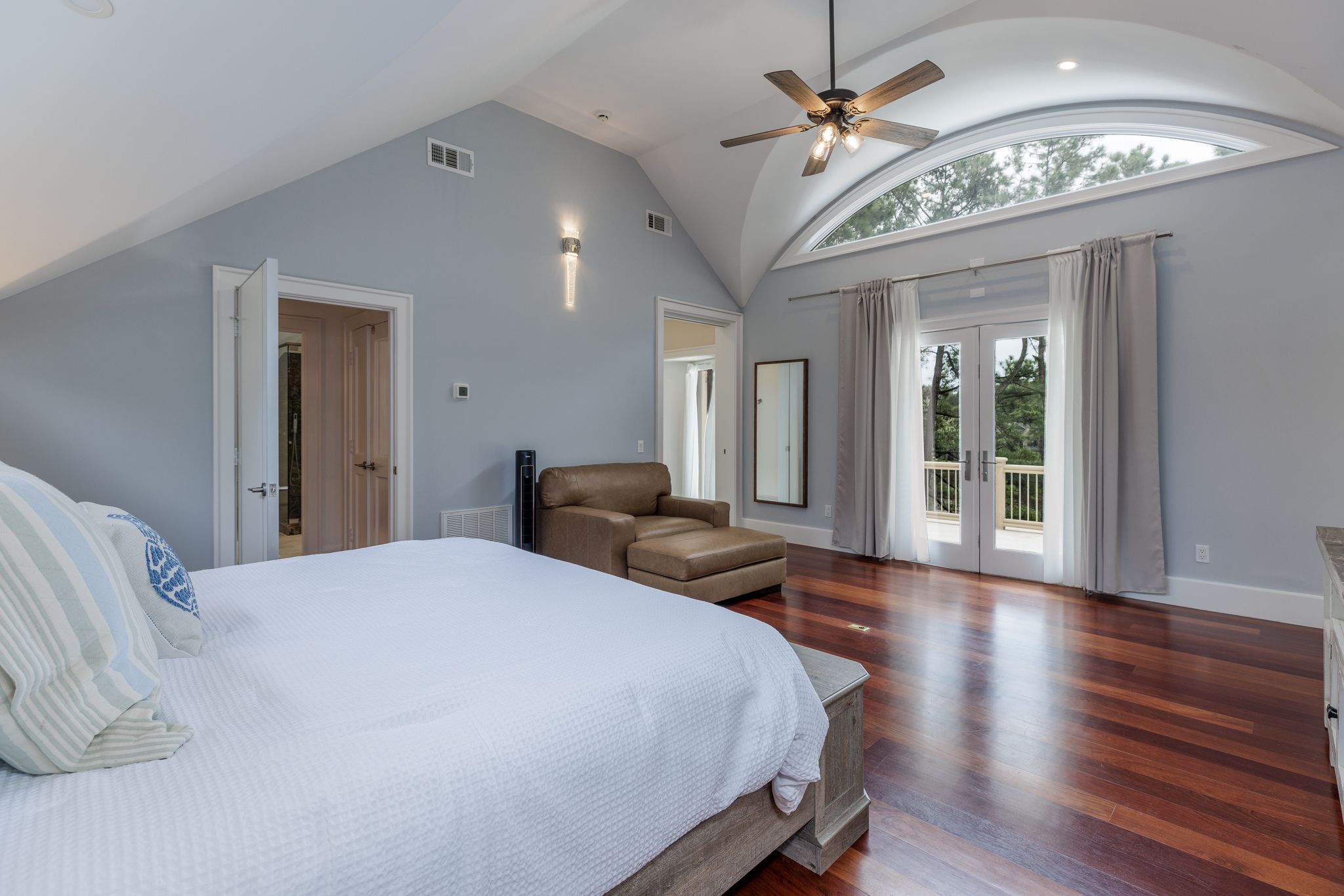 Primary suite with hardwood floors, arched window, and vaulted ceiling
