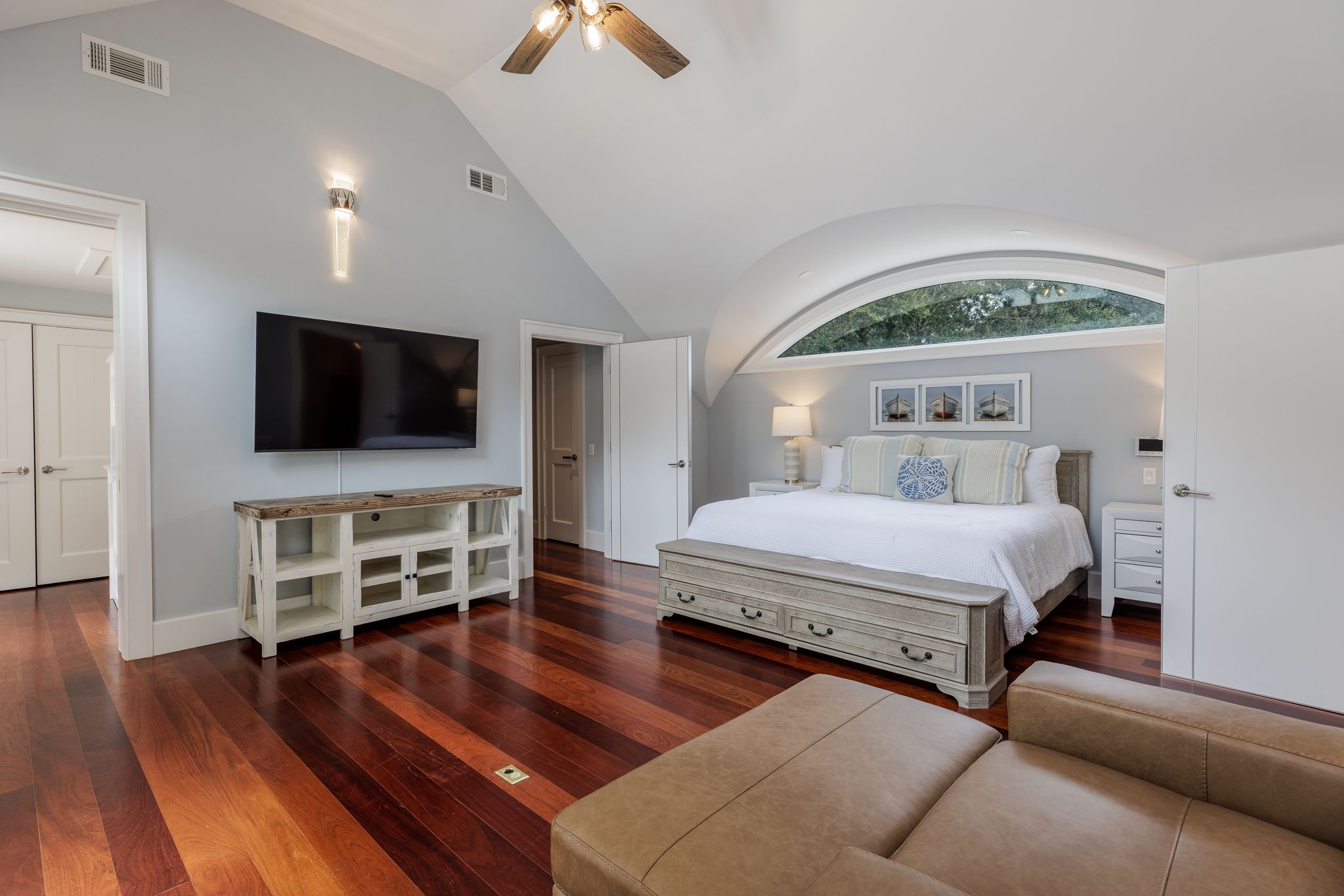 Primary suite with hardwood floors, a tall arched window, and a vaulted ceiling
