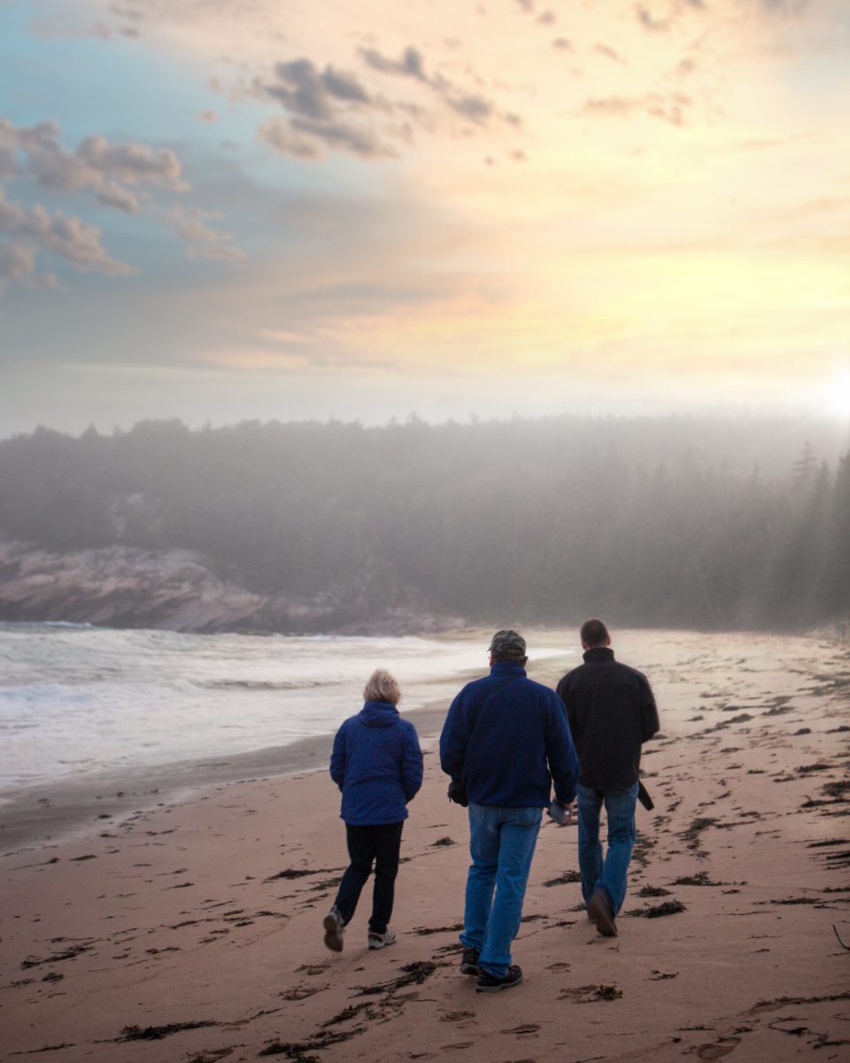 A family walking together along the shoreline at dusk.