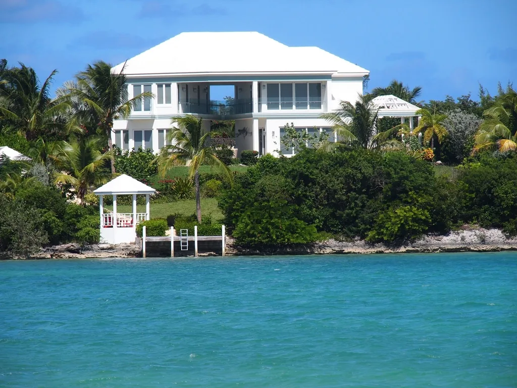 A large white waterfront vacation home with palms and a private dock on calm water.